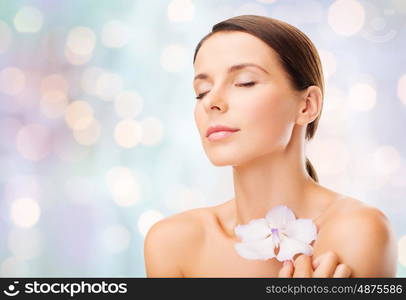 beauty, people, bodycare and health concept - beautiful young woman with orchid flower and bare shoulders over holidays lights background