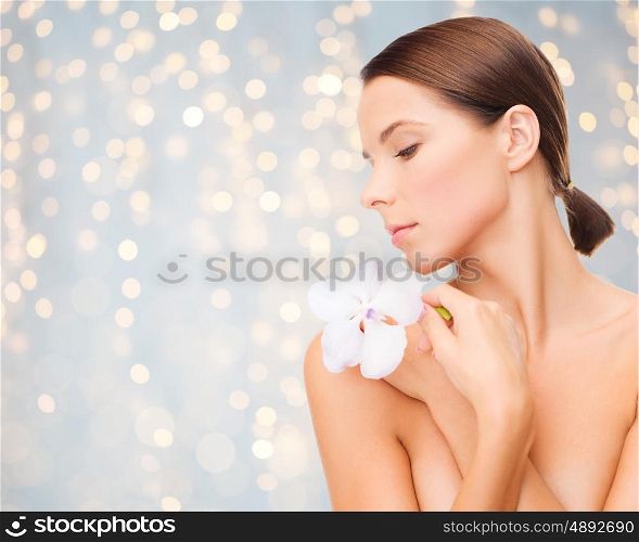 beauty, people, bodycare and health concept - beautiful young woman with orchid flower and bare shoulders over holidays lights background