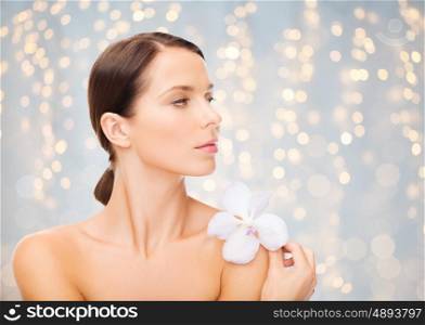 beauty, people, bodycare and health concept - beautiful young woman with orchid flower and bare shoulders over holidays lights background