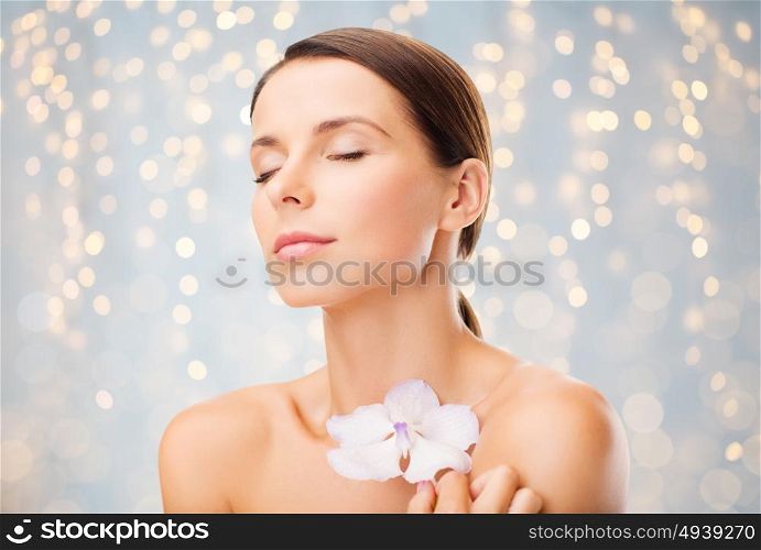 beauty, people, bodycare and health concept - beautiful young woman with orchid flower and bare shoulders over holidays lights background. beautiful young woman with orchid flower