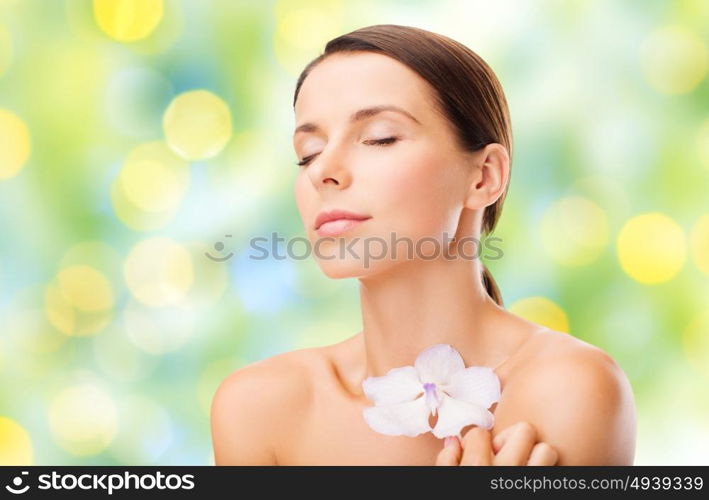 beauty, people, bodycare and health concept - beautiful young woman with orchid flower and bare shoulders over summer green lights background. beautiful young woman with orchid flower