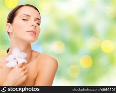 beauty, people, bodycare and health concept - beautiful young woman with orchid flower and bare shoulders over summer green lights background. beautiful young woman with orchid flower