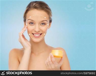 beauty, people, cosmetics, skincare and anti-aging concept - happy young woman applying cream to her face with white arrows over blue background