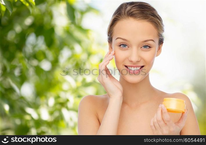 beauty, people, cosmetics, skincare and cosmetics concept - happy young woman applying cream to her face