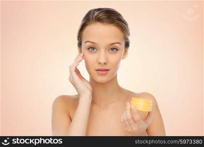 beauty, people, cosmetics, skincare and cosmetics concept - young woman applying cream to her face over beige background