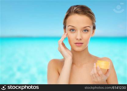 beauty, people, cosmetics, skincare and cosmetics concept - young woman applying cream to her face