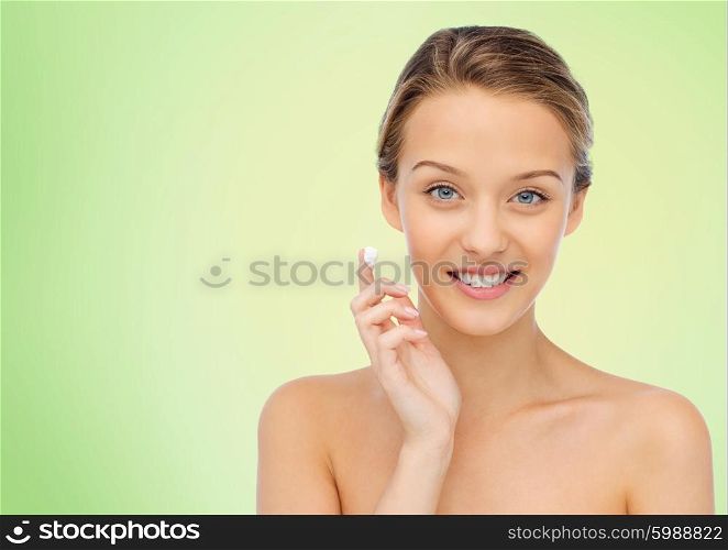 beauty, people, cosmetics, skincare and health concept - happy smiling young woman applying cream to her face over green natural background