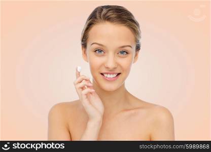 beauty, people, cosmetics, skincare and health concept - happy smiling young woman applying cream to her face over beige background