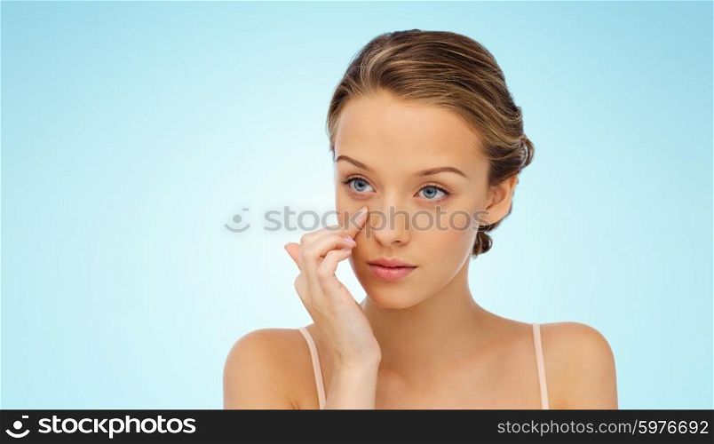 beauty, people, cosmetics, skincare and health concept - young woman applying cream to her face over blue background