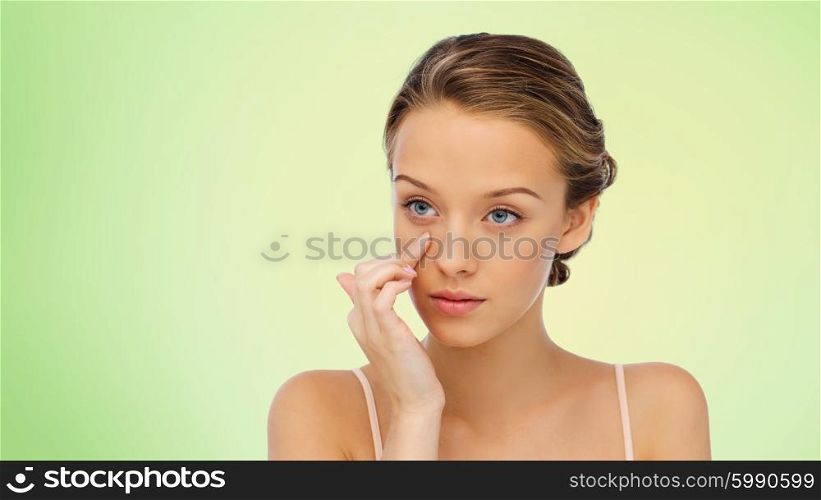 beauty, people, cosmetics, skincare and health concept - young woman applying cream to her face over green background