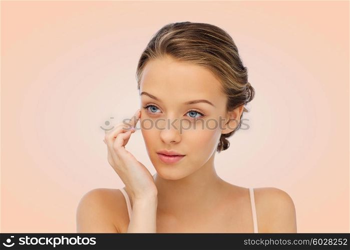 beauty, people, cosmetics, skincare and health concept - young woman applying cream to her face over beige background