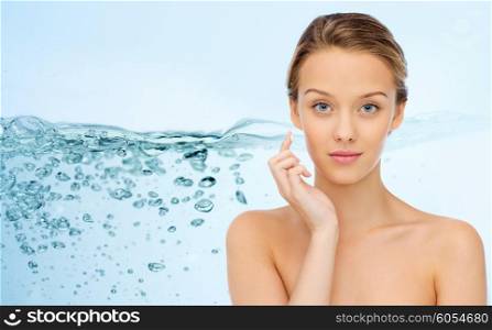 beauty, people, cosmetics, skincare and health concept - young woman applying cream to her face over water splash on blue background