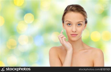 beauty, people, cosmetics, skincare and health concept - young woman applying cream to her face over green lights background