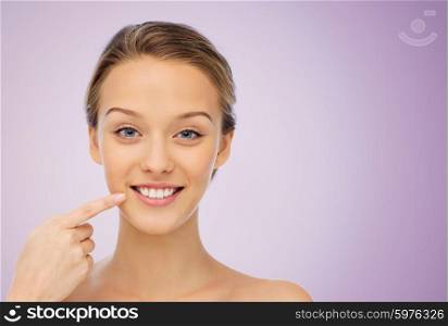 beauty, people, dental care and hygiene concept - happy young woman pointing finger to her smile or teeth over violet background