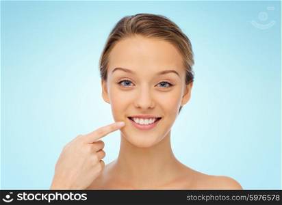 beauty, people, dental care and hygiene concept - happy young woman pointing finger to her smile or teeth over blue background