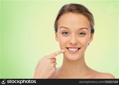 beauty, people, dental care and hygiene concept - happy young woman pointing finger to her smile or teeth over green background