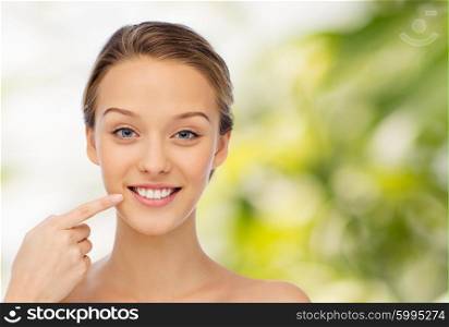 beauty, people, dental care and hygiene concept - happy young woman pointing finger to her smile or teeth over green natural background