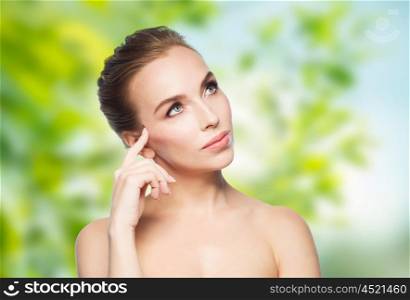 beauty, people, eco and health concept - beautiful young woman touching her face over green natural background
