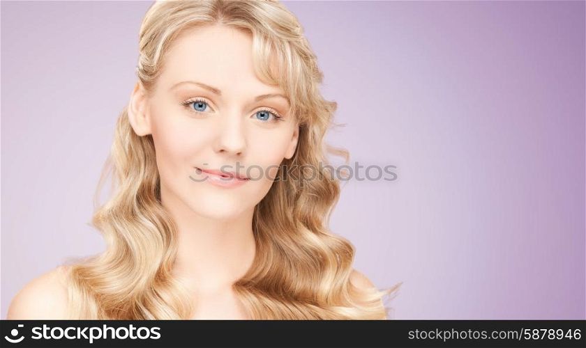 beauty, people, hair care and health concept - beautiful young woman face with long wavy hair over violet background