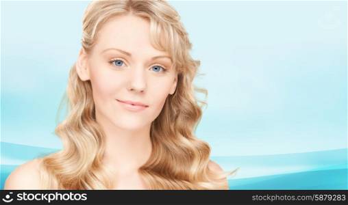 beauty, people, hair care and health concept - beautiful young woman face with long wavy hair over blue background