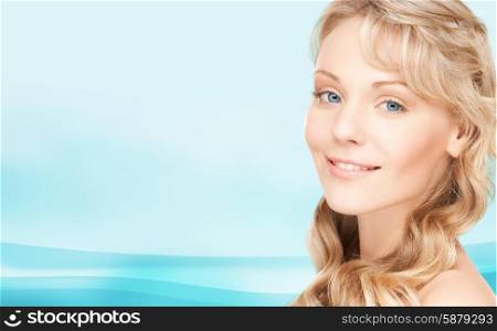 beauty, people, hair care and health concept - beautiful young woman face with long wavy hair over blue background