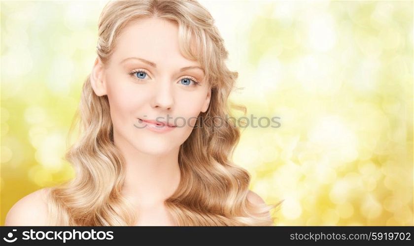 beauty, people, hair care and health concept - beautiful young woman face with long wavy hair over yellow lights background