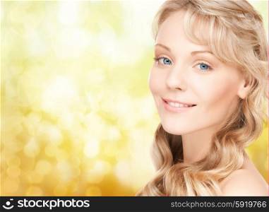 beauty, people, hair care and health concept - beautiful young woman face with long wavy hair over yellow lights background