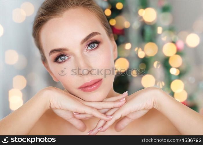 beauty, people, holidays and bodycare concept -beautiful young woman face and hands over christmas tree lights background