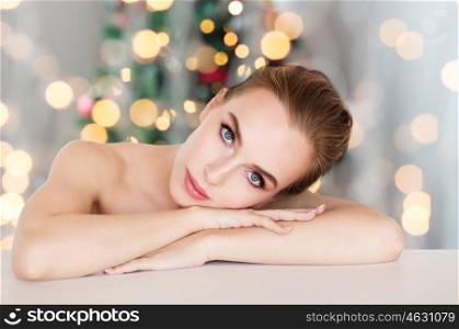 beauty, people, holidays and bodycare concept -beautiful young woman face and hands over christmas tree lights background