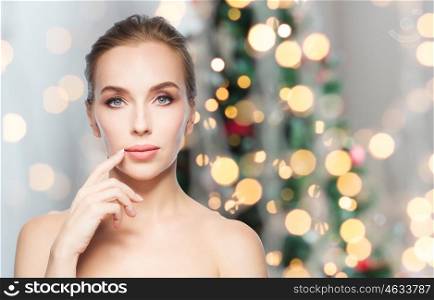 beauty, people, holidays and plastic surgery concept - beautiful young woman showing her lips over christmas tree lights background
