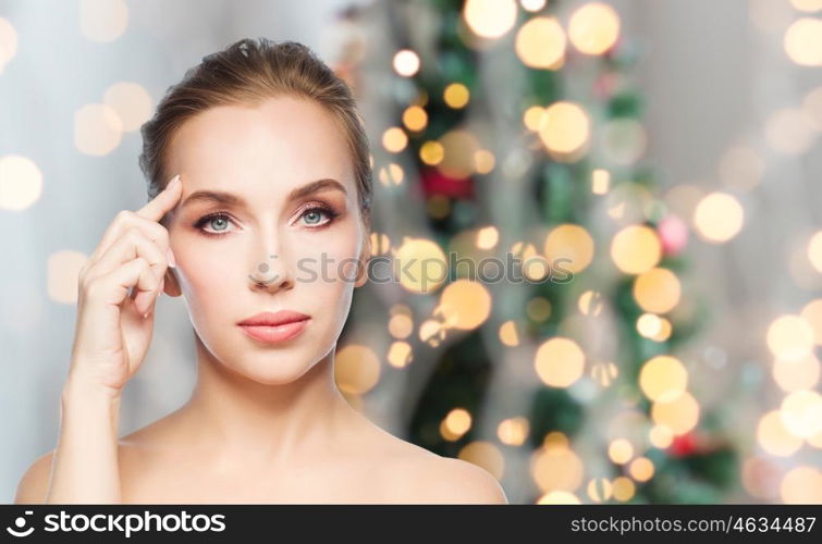 beauty, people, holidays and plastic surgery concept - beautiful young woman showing her forehead over christmas tree lights background