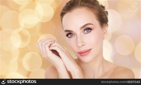 beauty, people, holidays and skin care concept - beautiful young woman face and hands over beige lights background