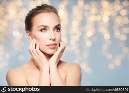 beauty, people, holidays and skin care concept - beautiful young woman touching her face over lights background