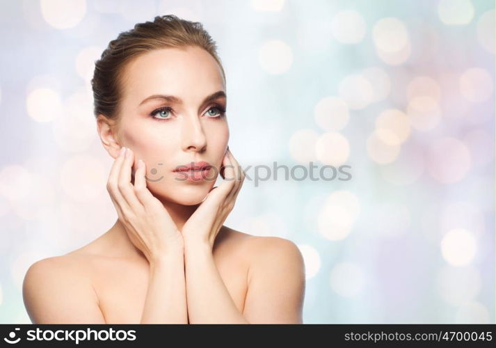 beauty, people, holidays and skin care concept - beautiful young woman touching her face over lights background