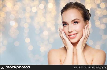 beauty, people, holidays and skin care concept - beautiful young woman touching her face over lights background