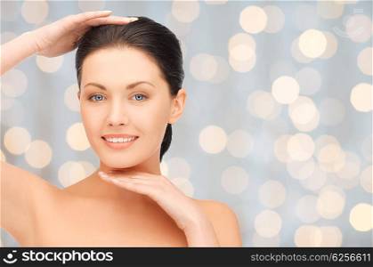 beauty, people, holidays, luxury and health concept - beautiful young woman touching her face and chin over lights background