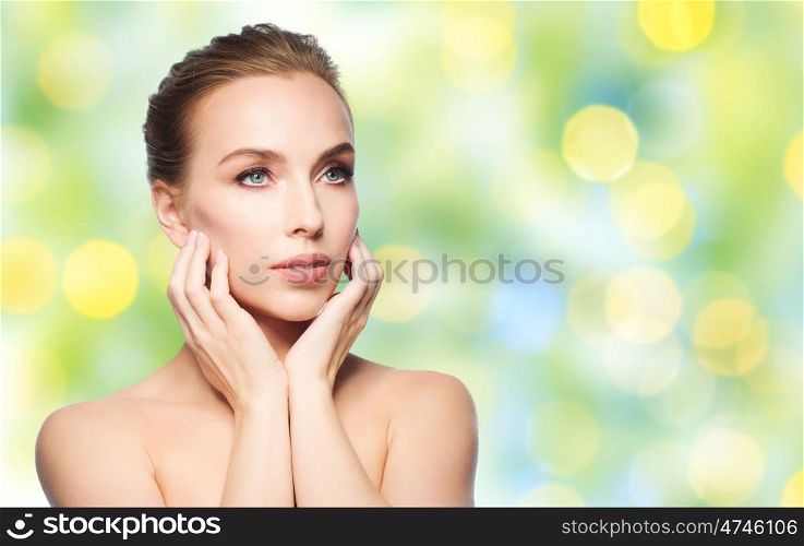 beauty, people, holidays, summer and skin care concept - beautiful young woman touching her face over green lights background