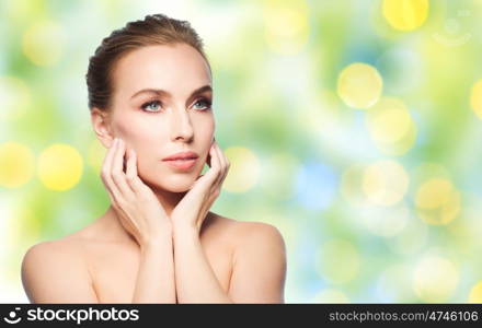 beauty, people, holidays, summer and skin care concept - beautiful young woman touching her face over green lights background