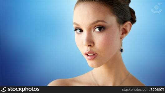 beauty, people, make up and luxury concept - close up of beautiful asian woman or bride with earring over blue background