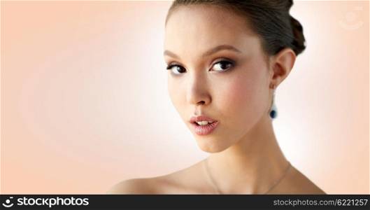 beauty, people, make up and luxury concept - close up of beautiful asian woman or bride with earring over beige background
