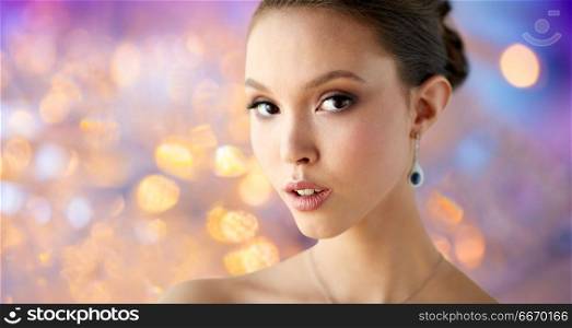 beauty, people, make up and luxury concept - close up of beautiful asian woman or bride with earring over holidays lights background. close up of beautiful woman face with earring. close up of beautiful woman face with earring