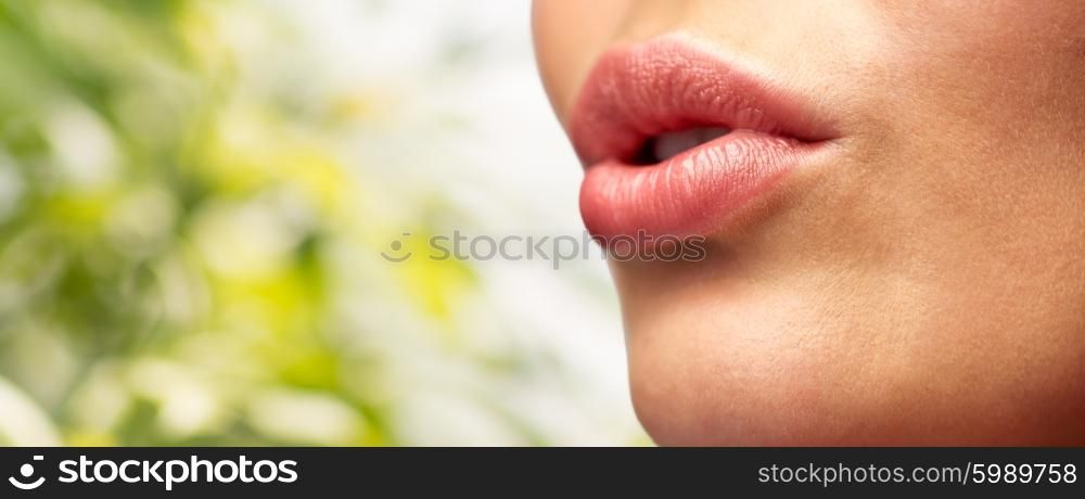 beauty, people, make-up and plastic surgery concept - close up of young woman lips over green natural background