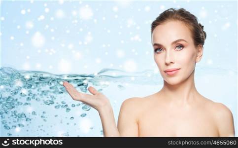 beauty, people, moisturizing, advertisement and skin care concept - smiling young woman holding something on palm of her hand over water splash bubbles on blue background and snow