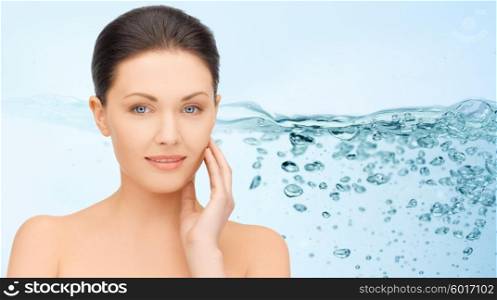 beauty, people, moisturizing and health concept - smiling young woman with bare shoulders touching her face over water splash on blue background