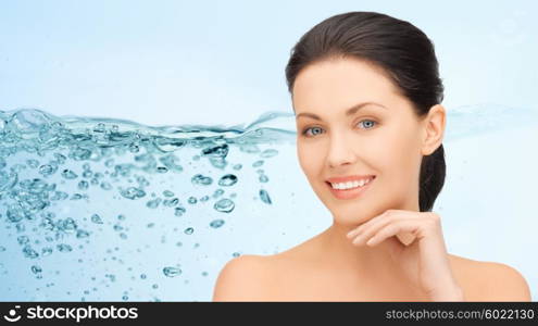 beauty, people, moisturizing and health concept - smiling young woman with bare shoulders touching her face over water splash on blue background