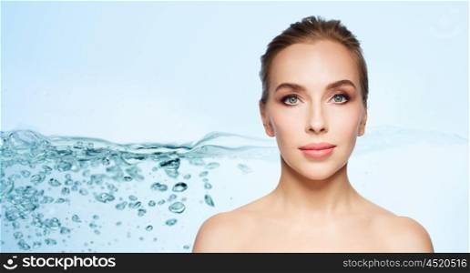 beauty, people, moisturizing and skincare concept - beautiful young woman face over blue background with water splash