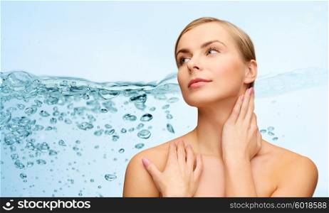 beauty, people, moisturizing, body care and health concept - young woman with bare shoulders touching her neck over water splash on blue background