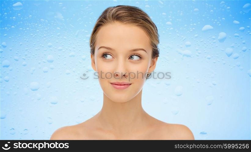 beauty, people, moisturizing, skin care and health concept - smiling young woman face and shoulders over water drops on blue background