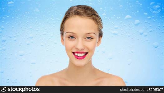 beauty, people, moisturizing, skin care and health concept - smiling young woman face with pink lipstick on lips and shoulders over water drops on blue background