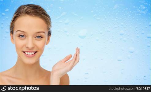 beauty, people, moisturizing, skin care and health concept - smiling young woman face and shoulders over water drops on blue background